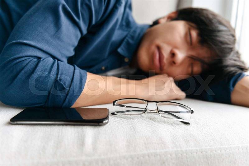 Tired asian man sleeping on a couch with mobile phone, stock photo