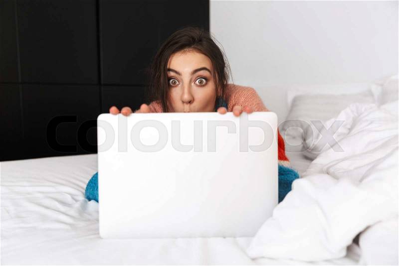 Photo of funny woman 30s lying on couch in apartment, and using silver laptop, stock photo