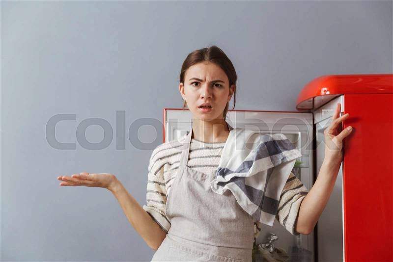 Confused young woman standing at the fridge in kitchen at home, stock photo