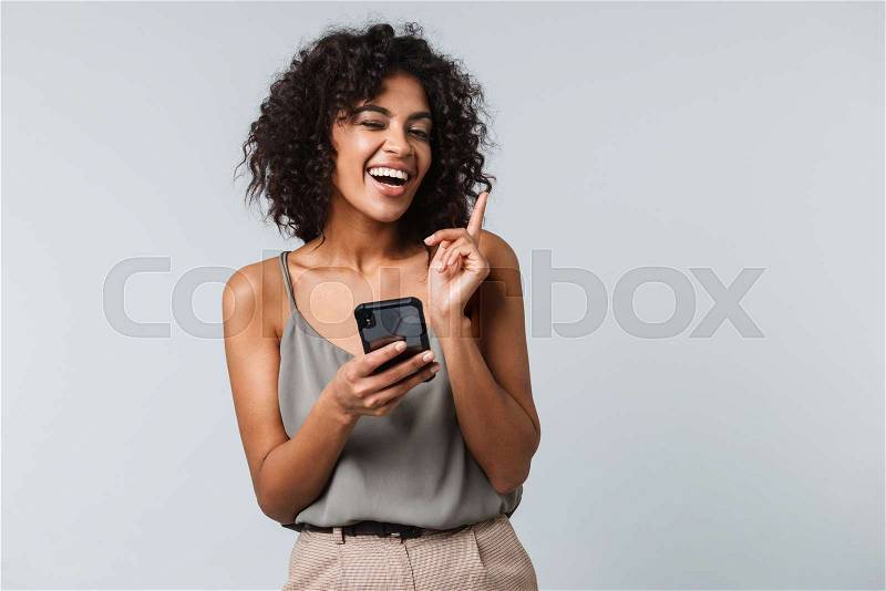 Happy young african woman casually dressed standing isolated over gray background, using mobile phone, stock photo