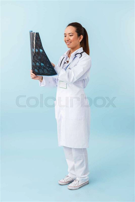 Photo of a young happy woman doctor posing isolated over blue wall background with x-ray, stock photo