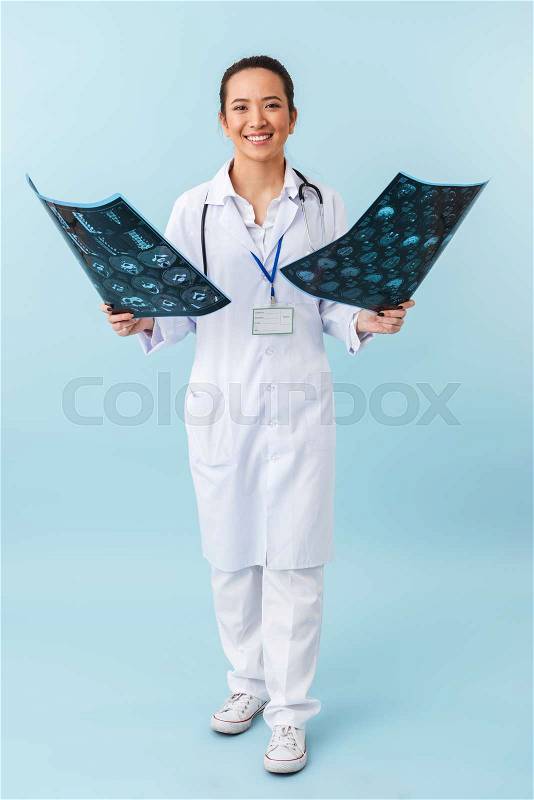 Photo of a young happy woman doctor posing isolated over blue wall background with x-ray, stock photo