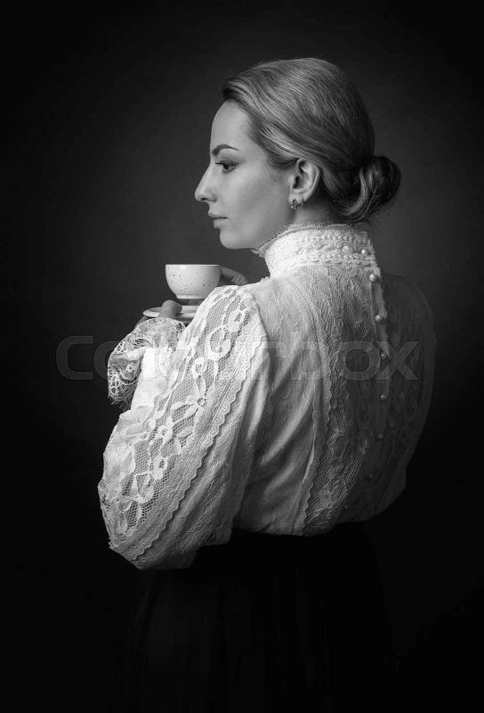 Portrait of a woman in Victorian clothes with a cup of coffee. White blouse with lace, embroidery and high collar. Black background, stock photo
