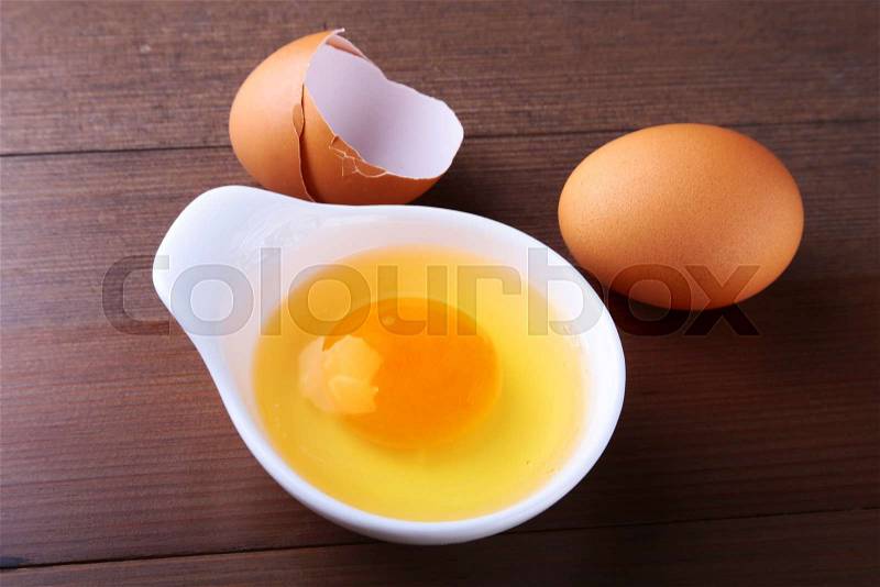 Egg yolk in a white bowl and raw egg on the table. ingredients for cooking. concept. View from above, stock photo