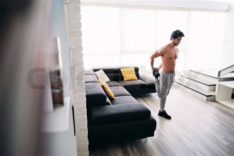 Bare chested young man stretching muscles before starting a workout routine. Handsome hispanic male athlete exercising for wellness in his living room. Latino people ..., stock photo