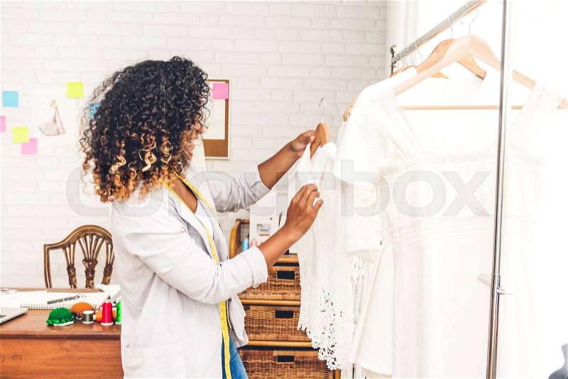 Smiling african american black woman fashion designer standing working and holding dress at workshop studio, stock photo
