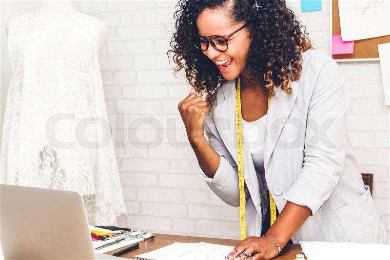 Smiling african american black woman fashion designer standing and working with laptop computer at workshop studio, stock photo