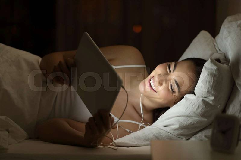 Happy woman watching movie on a tablet in the night on a bed at home, stock photo
