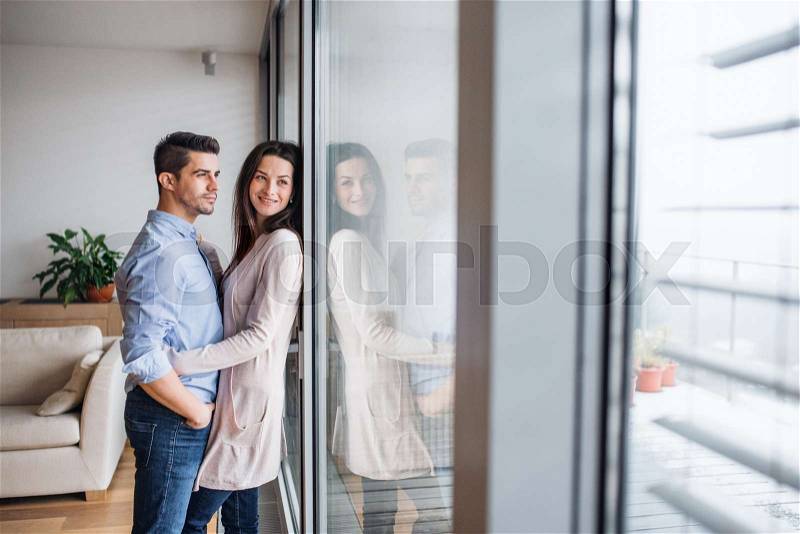 Young happy couple in love standing by the window at home, hugging. Copy space, stock photo
