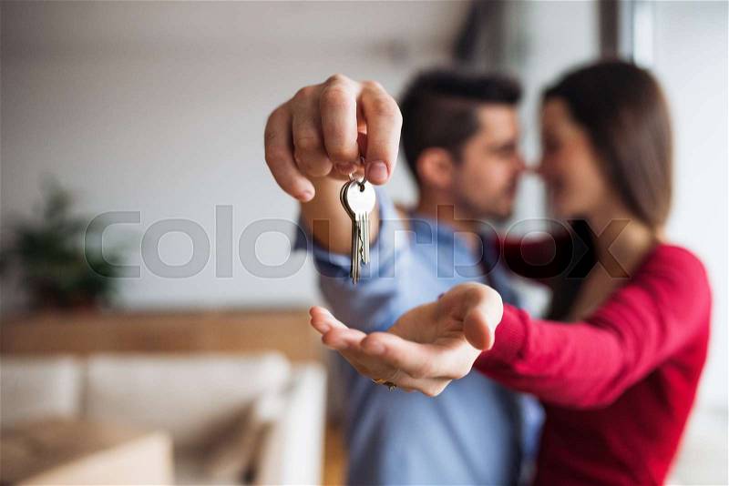 A young happy couple with a key and cardboard boxes standing indoors, moving in a new home, stock photo