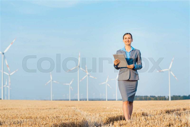 Women putting money into an ethical Investment of wind turbines, standing with her computer on a field, stock photo