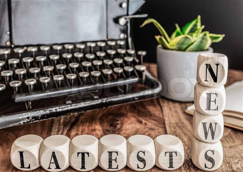 Close-up of words LATEST NEWS on wooden blocks with vintage typewriter and potted plant in background, stock photo