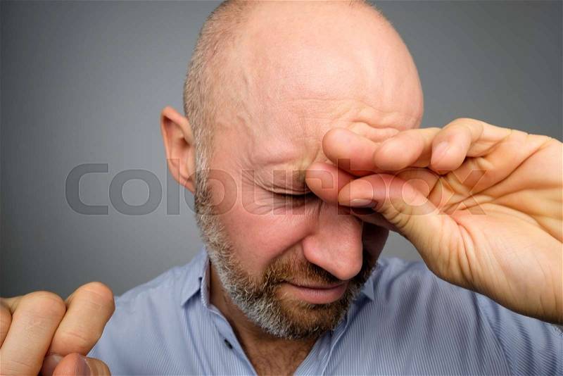 Good-looking caucasian man suffering from pain and eye pain isolated on gray background. He is showing how much his head hurts, experiencing pain, looking miserable ..., stock photo