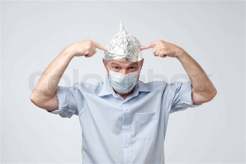 Caucasian mature man in a tin foil hat and medical hat displeased hiding from outdoor life. Afraid of radiation or aliens. Stop sign, stock photo