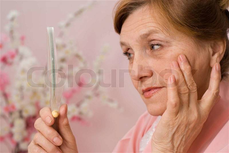 Happy elderly woman looks in the mirror, stock photo