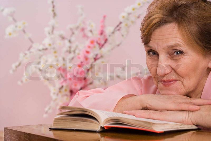 Woman sitting at a table reading a book and dreams, stock photo