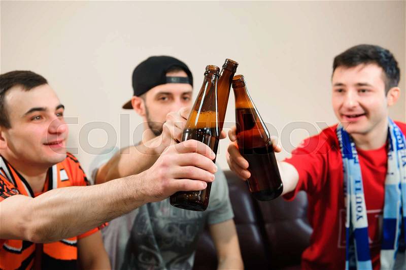 Young men drink beer, eat chips and root for football, stock photo