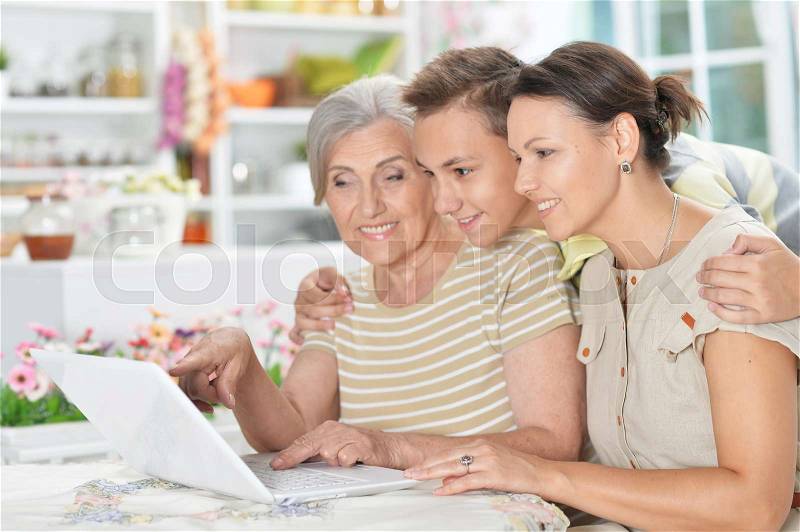 Smiling grandmother, mother and son using laptop at home, stock photo