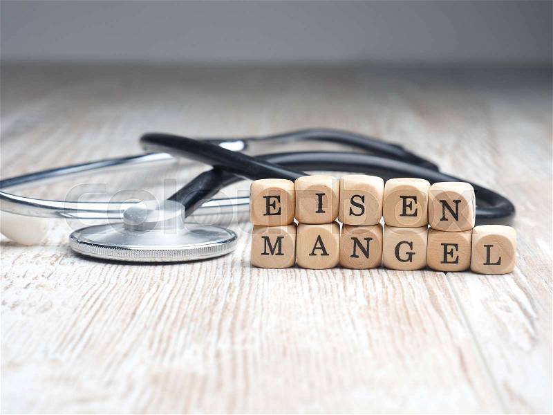 The German words iron deficiency on small wooden blocks with a stethoscope on a table, health care or medical concept, stock photo