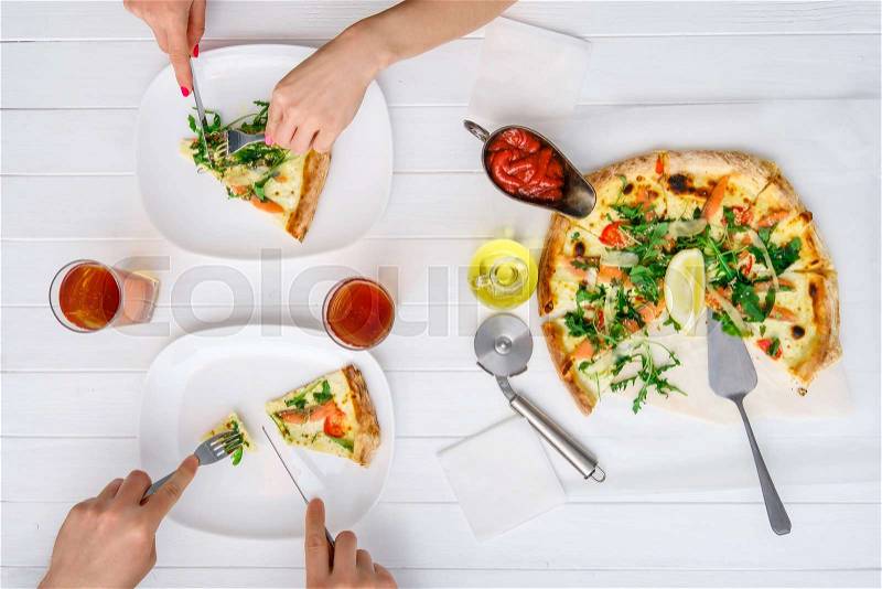 Couple eating pizza freshly cooked pizza with drinks on white wood table, stock photo