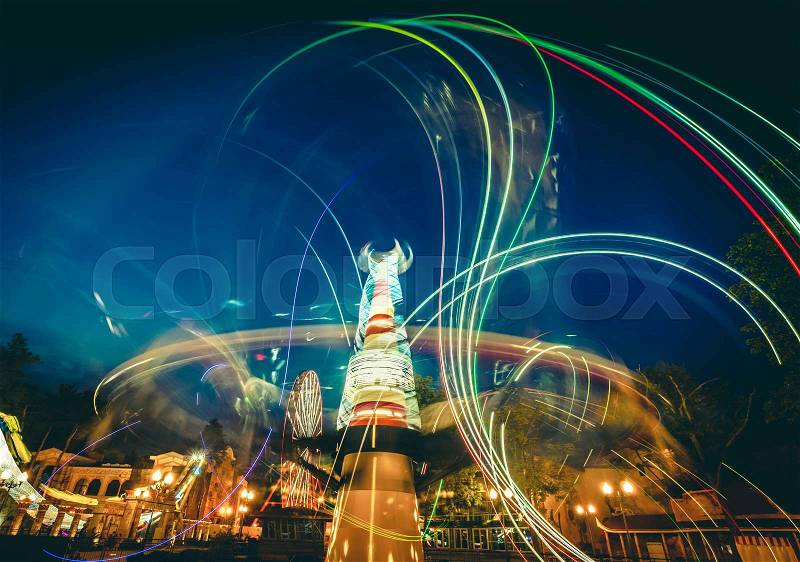 Abstract bright neon light trails of carousels in luna park at twilight, stock photo