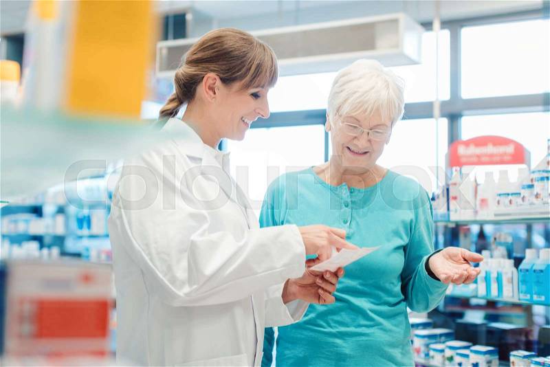 Pharmacist servicing senior customer in her pharmacy holding bottle with pills in her hand , stock photo