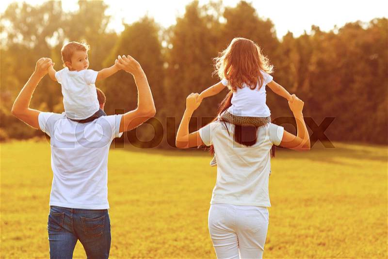 View from behind. A family with children are walking on the grass in a park in the summer in the autumn, stock photo