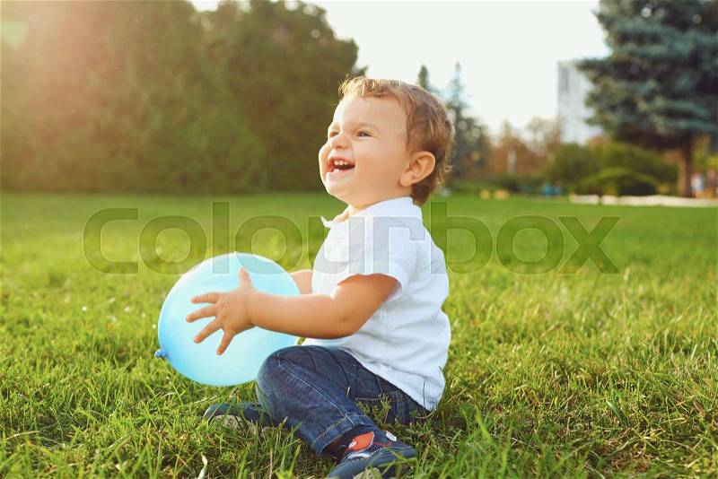 Little boy with a balloon plays, smiles on the grass in the park. Children\'s Day, stock photo