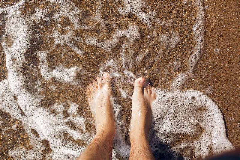 Top view of person feet in water on sandy beach and waves. Summer vacation concept. Relaxing at ocean shore, stock photo