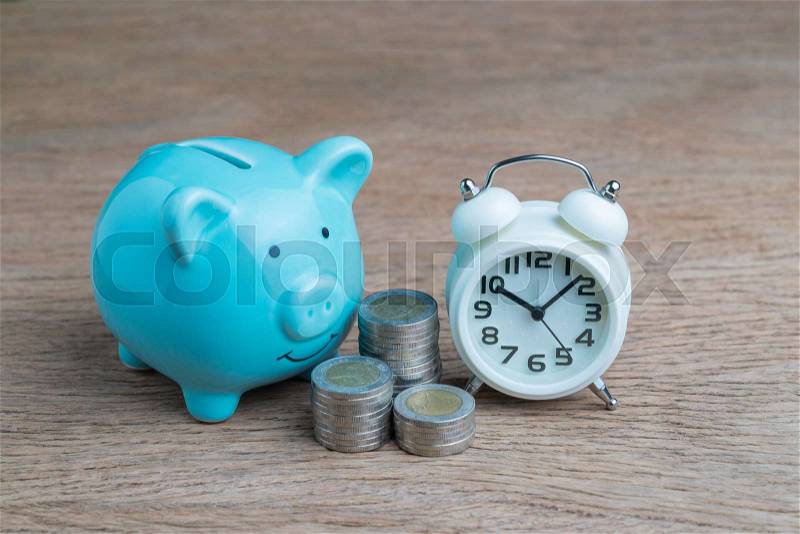 Financial long term saving money, debt control concept, blue piggy bank, coins stacked and alarm clock on wood table, compound interest of investment awareness, stock photo