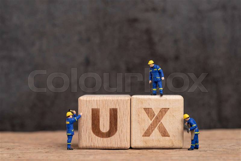 User Experience design in product and service concept, miniature people workers with blue team uniform building cube wooden block with acronym UX on table with ..., stock photo