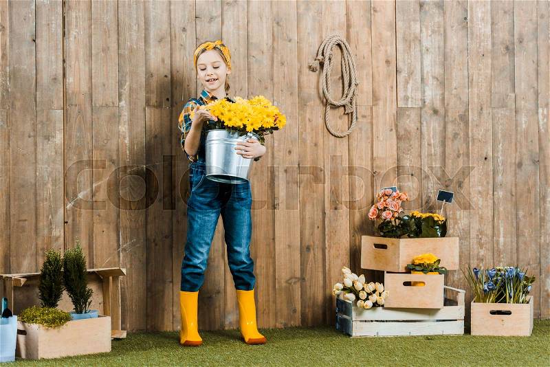 Cheerful kid holding flowers in bucket near boxes with plants, stock photo