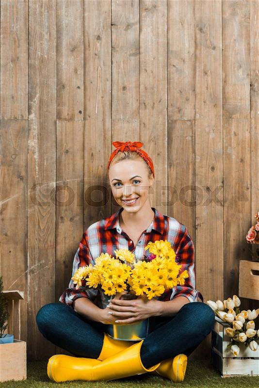 Happy woman sitting with crossed legs and holding flowers in bucket, stock photo