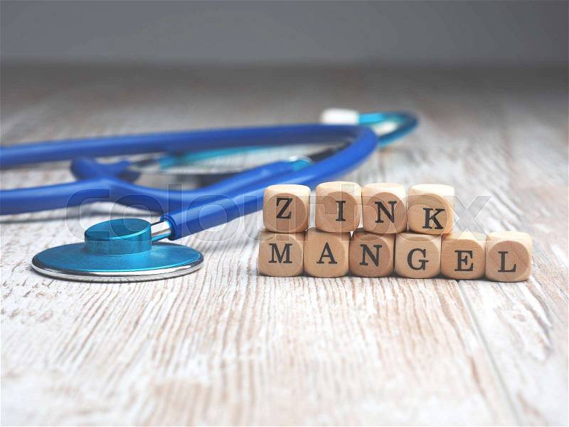 The German words zinc deficiency on small wooden blocks with a stethoscope on a table, health care or medical concept with space for text, stock photo