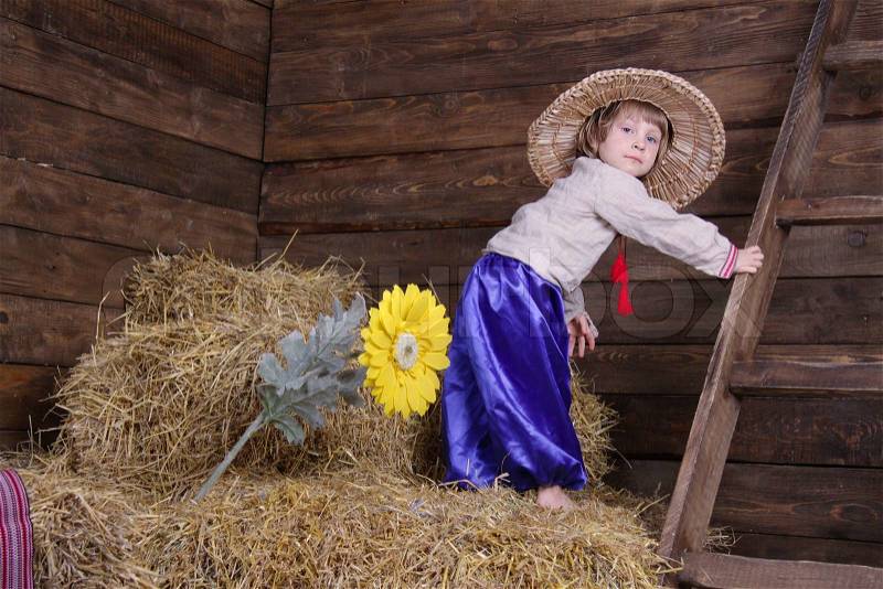 Cute child in traditional eastern european clothes on hayloft, stock photo