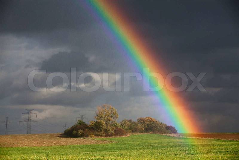 Natural rainbow over green field and dark sky, stock photo