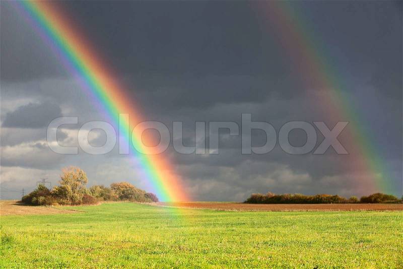 Natural two rainbow over green field and dark sky, stock photo