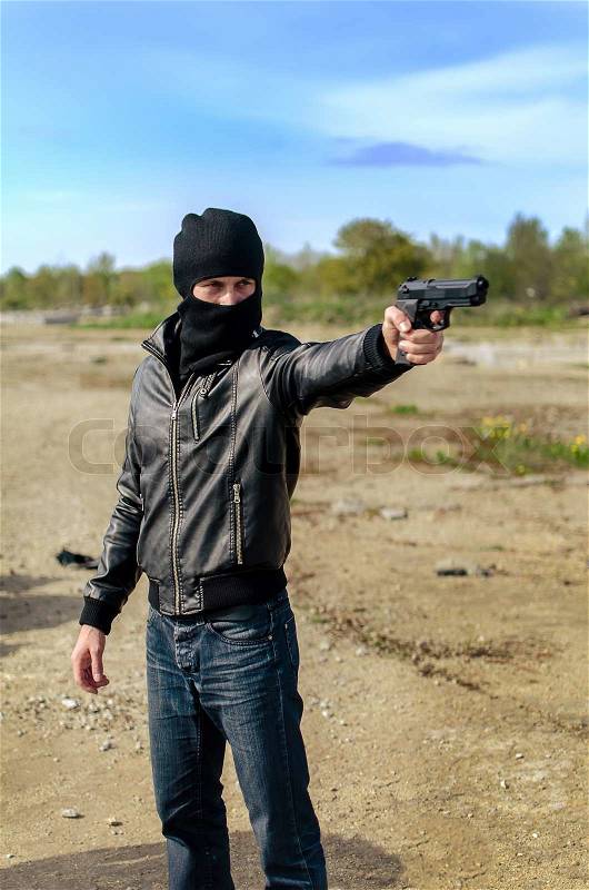 Masked gunman taking aim with a gun, stock photo