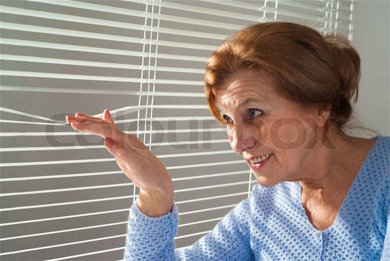 An elderly woman looks out the window, stock photo