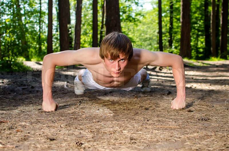 Attractive man doing a push up in forest, stock photo