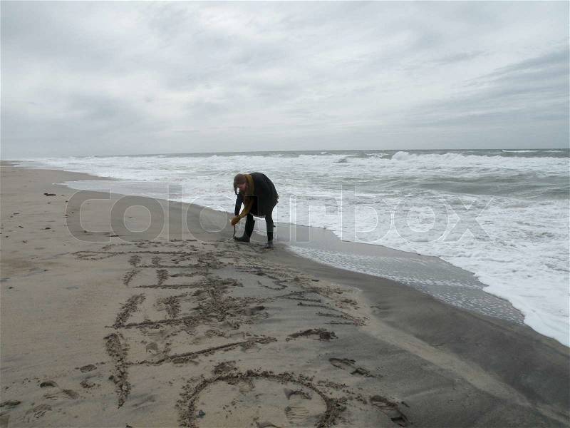 Girl writing something into the wet sand at Beach in thy national park on a cloudy day at northsea, jutland, denmark, scandinavia, stock photo