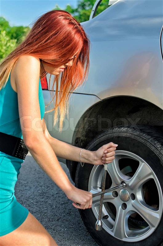 Pretty girl removing a wheel on a road, stock photo