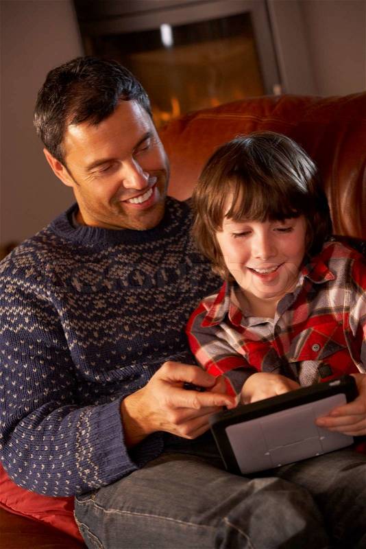 Father And Son Using Tablet Computer By Cosy Log Fire, stock photo