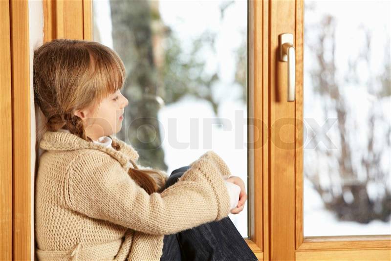 Young Girl Sitting On Window Ledge Looking At Snowy View, stock photo