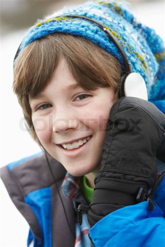 Boy Wearing Headphones And Listening To Music Wearing Winter Clothes In Snowy Landscape, stock photo