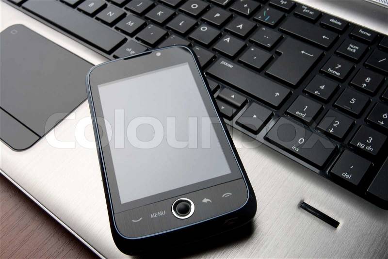 Modern phone with touchscreen on laptop keyboard, stock photo