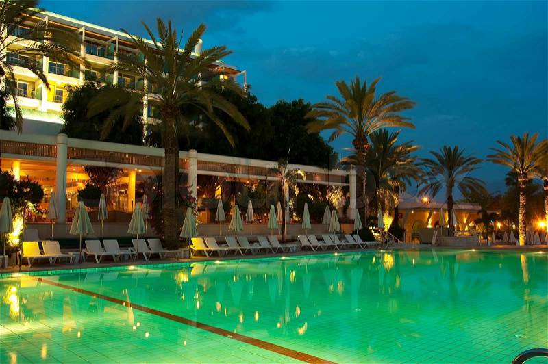 Night swimming pool against the backdrop of palm trees and hotels, stock photo