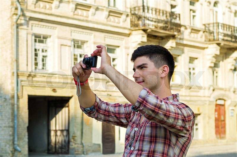 Young man standing taking photographs with a compact camera outside an old historical building, stock photo