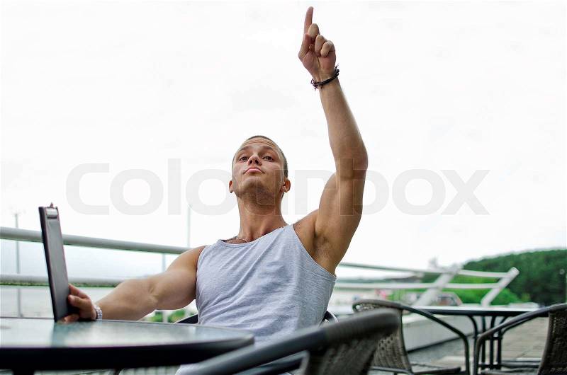 Handsome muscular male orders food in summer cafe Calling a waiter, stock photo