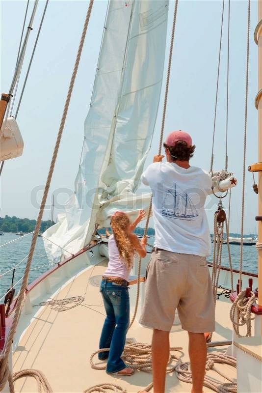 Girl helping a crew member to raise a sail, stock photo